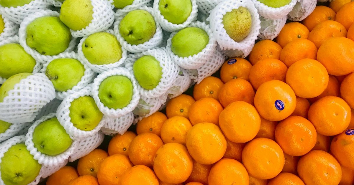 Green pears in white styrofoam holders and mandarin oranges. They are stacked right next to each other.